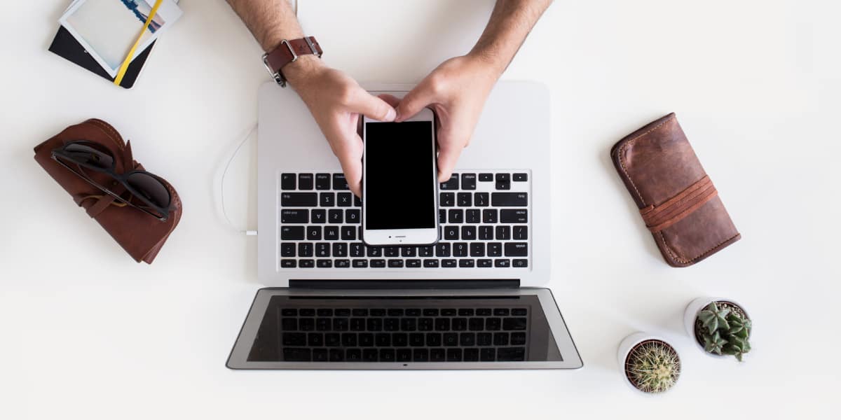 hands holding mobile phone above laptop