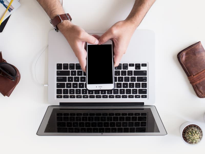 hands holding mobile phone above laptop